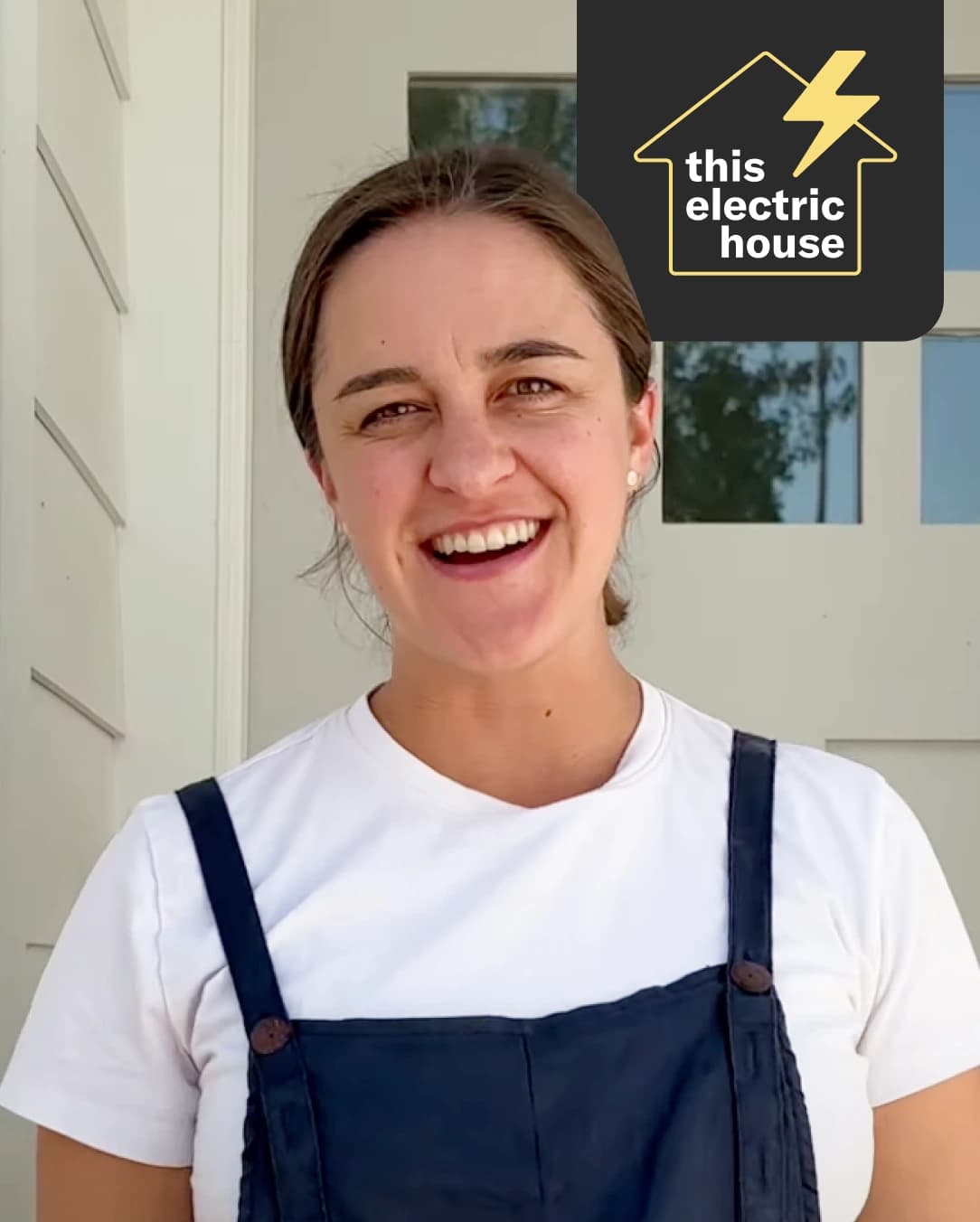 Photo of Cora Wyent in front of her house. She has light brown hair pulled back into a bun, and wears a white tshirt and navy overalls.