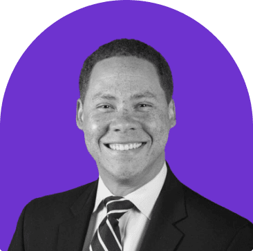 Black and white headshot of Matt Martin, who wears a suit with a black and white striped tie. He is smiling and has short curly hair.