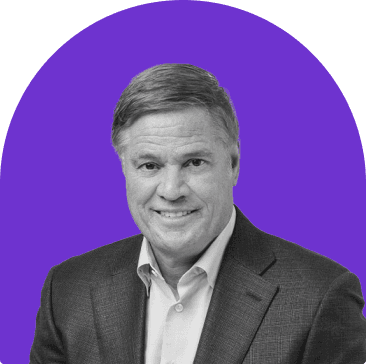 Black and white headshot of Tracy K. Price,  who is smiling and wears a white collared button up with a grey suit jacket. He has short hair. The headshot is on a purple curved rectangle background.
