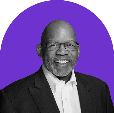 Black and white headshot of Kevin Walker, who is smiling and wears a white collared button up with a suit jacket. He is bald and wears thin framed glasses. The headshot is on a purple curved rectangle background.