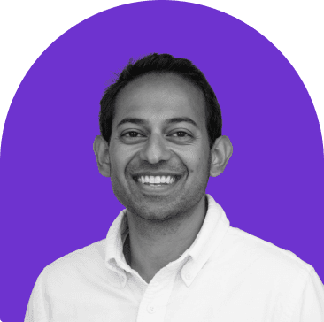 Black and white headshot of Kiran Bhatraju, who is smiling and wears a white collared button up shirt. He has short black hair. The headshot is on a purple curved rectangle background.