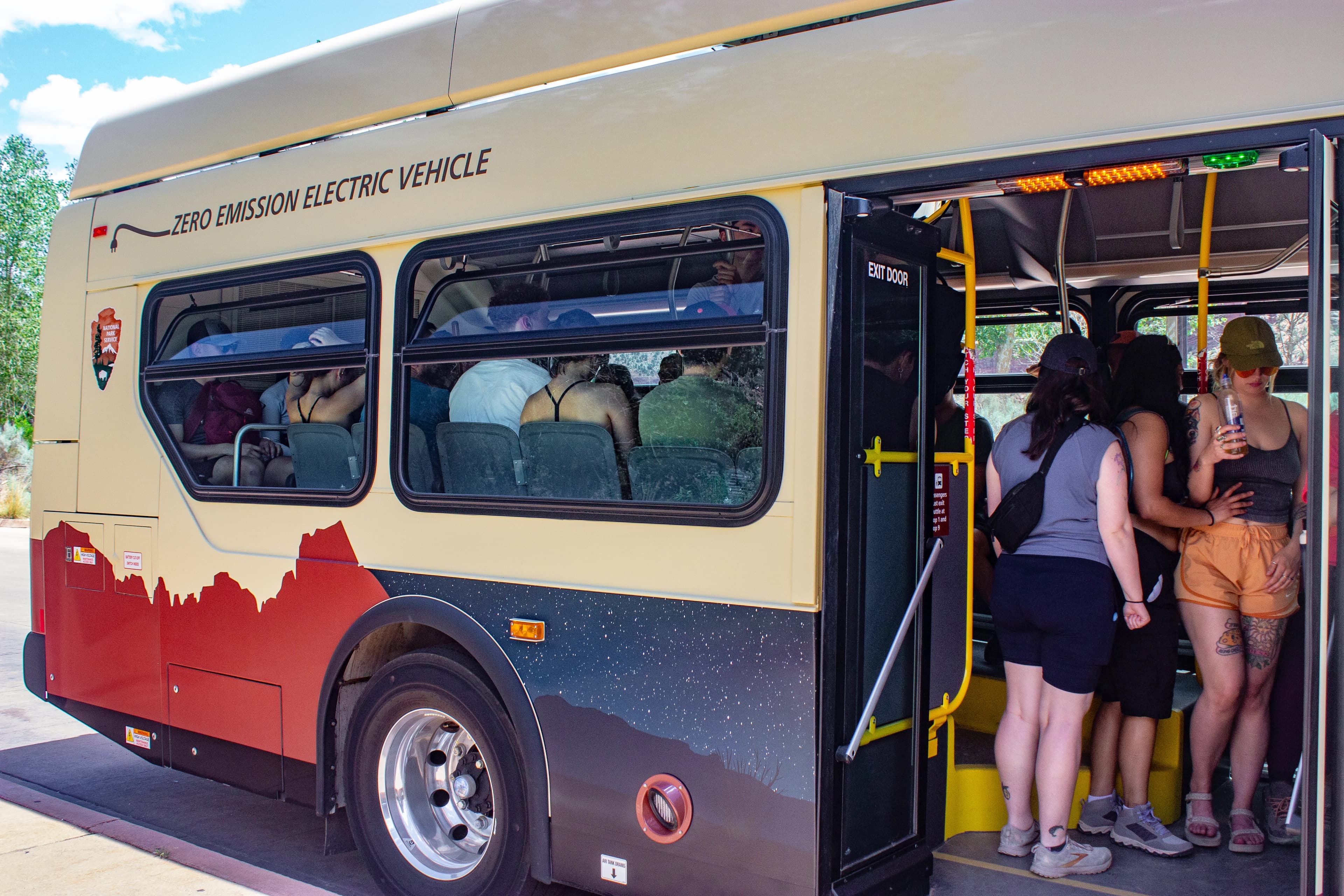 People boarding a zero-emission electric bus with a mountain design on its side. Some passengers are seated inside, and others are entering.