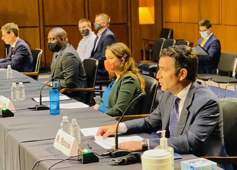 Rewiring America CEO Ari Matusiak, and Rewiring advisors Dr. Leah Stokes of UC Santa Barbara and Donnel Baird of BlocPower sitting at a table in front of microphones. Matusiak is wearing a navy gray suit with a navy tie, Stokes is wearing a blue top with a gray green cardigan.